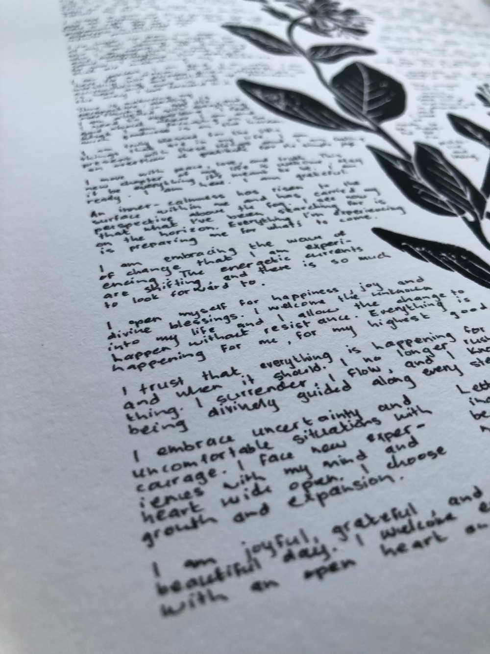 Close up of a lino print of a honeysuckle flower surrounded by tiny handwritten positive affirmations photographed from the bottom corner of the print.