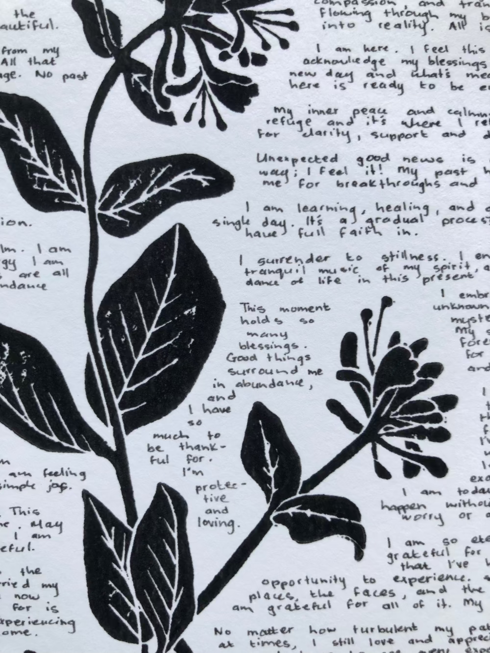 Close up of a lino print of a honeysuckle flower surrounded by tiny handwritten positive affirmations.