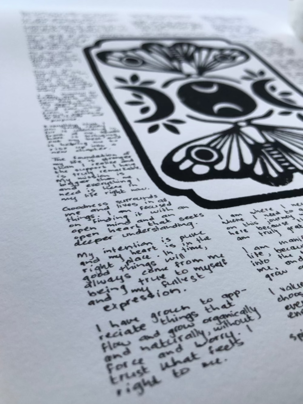 Close up of a lino print of moths and moons surrounded by tiny handwritten positive affirmations, photographed from the bottom corner of the print.