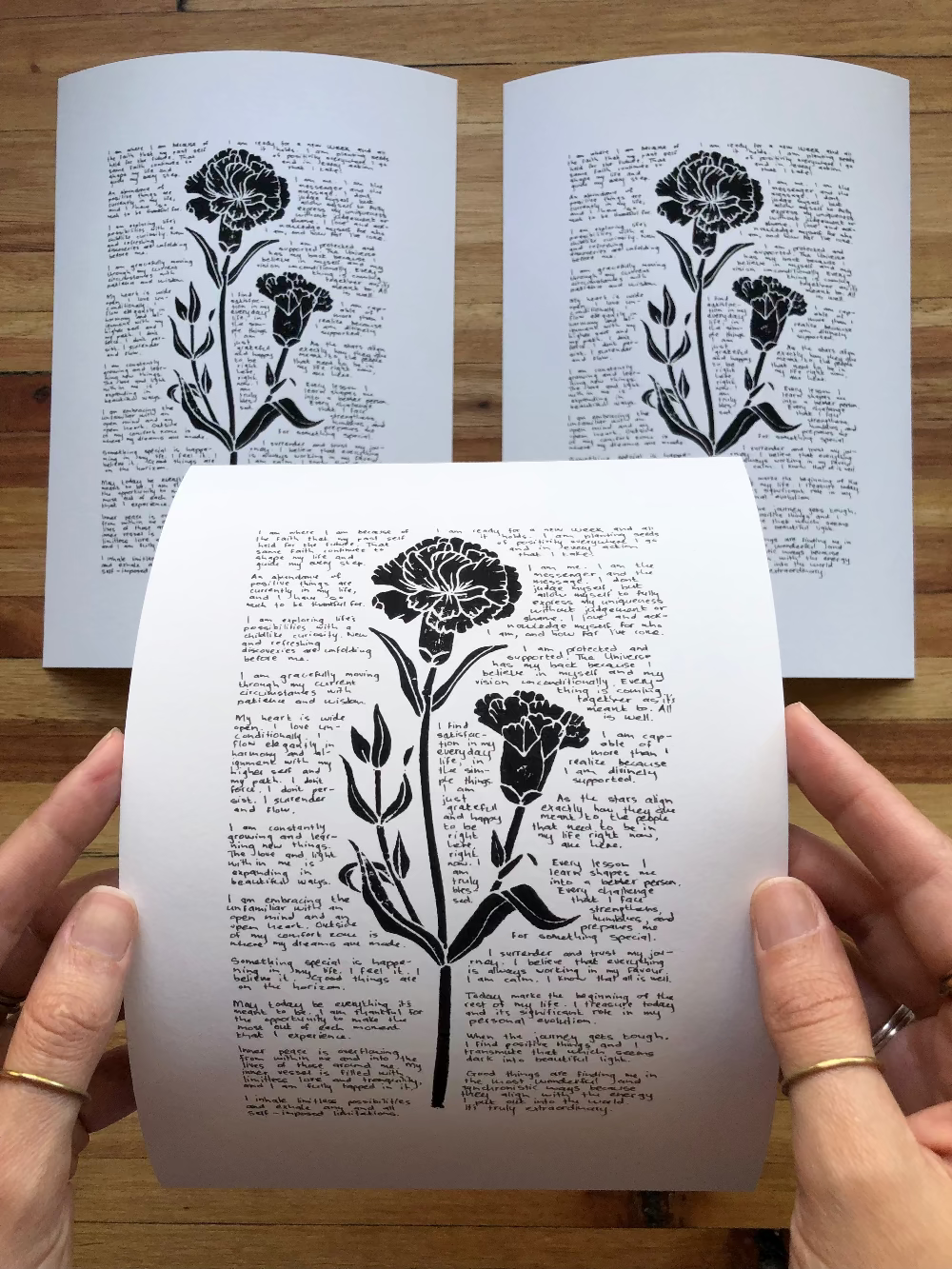 Three prints are photographed together on a table, one is being held by a person to show perspective.