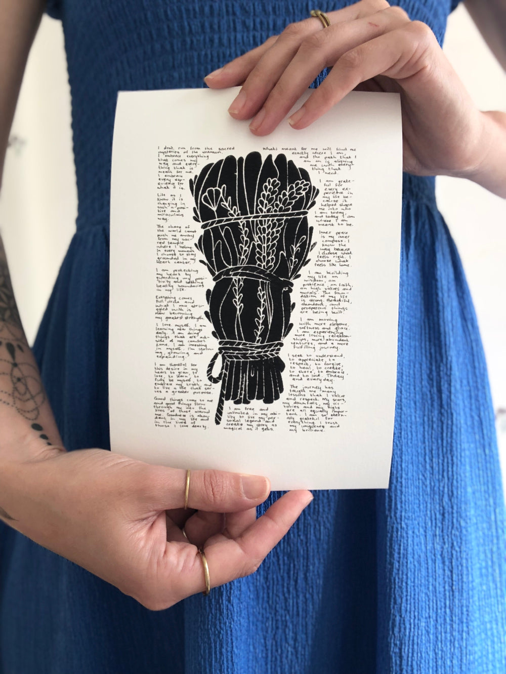 Artist holding the print of a black lino print surrounded with tiny handwritten positive affirmations.