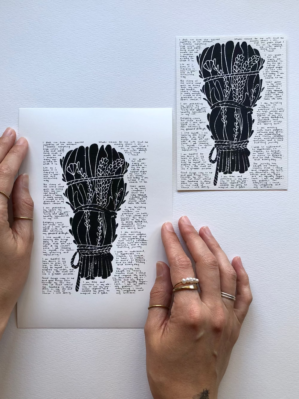 Black lino fine art print surrounded with tiny handwritten positive affirmations photographed flat on the table next to the original.