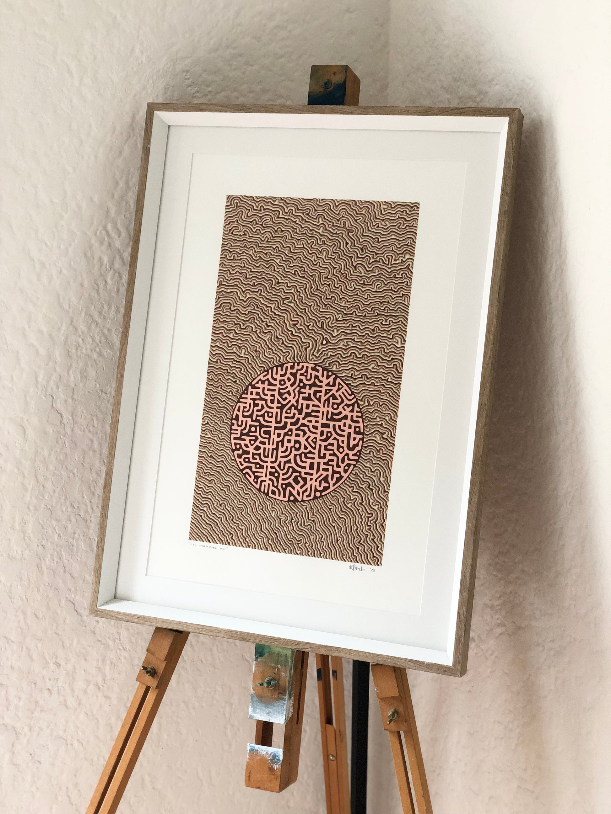 Framed abstract artwork on an easel against a beige wall