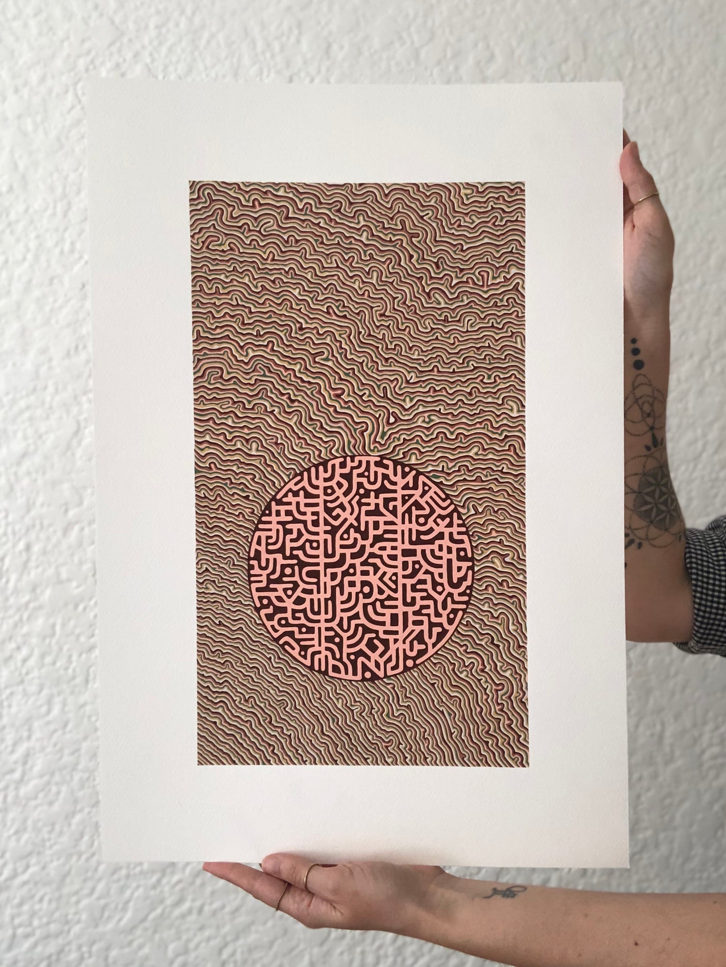 Abstract artwork with wavy patterns and a central circle design held by the artist against a textured white wall.
