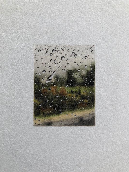 A blurry landscape with raindrops on a glass surface.